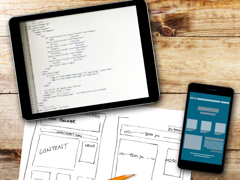 website wireframe sketch and programming code on digital tablet